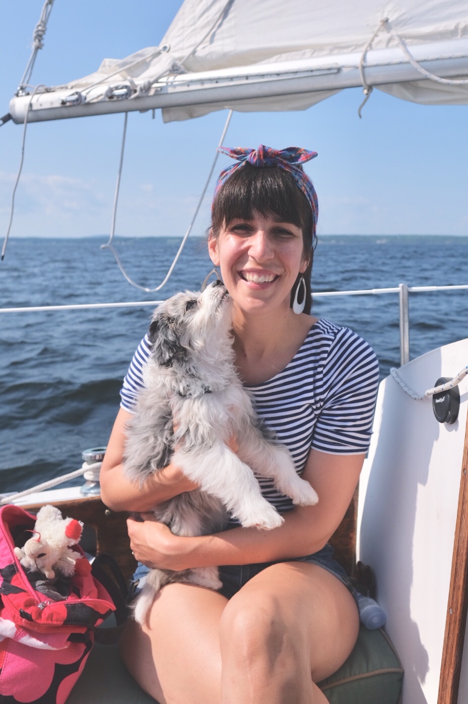 woman on a sailboat wearing headband with AussieDoodle puppy giving kisses.
