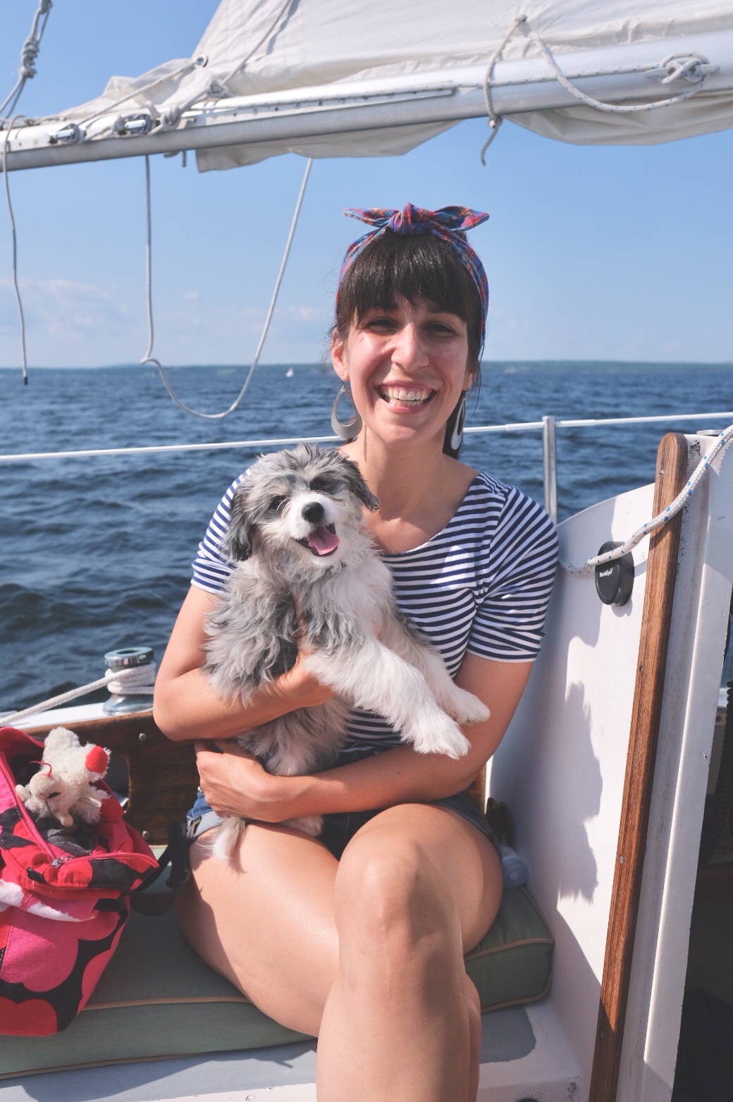 Smiling woman on a sailboat wearing headband with smiling AussieDoodle puppy.