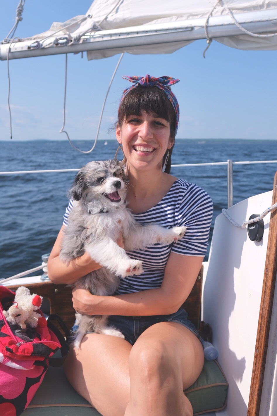 Smiling woman on a sailboat wearing headband with smiling AussieDoodle puppy.